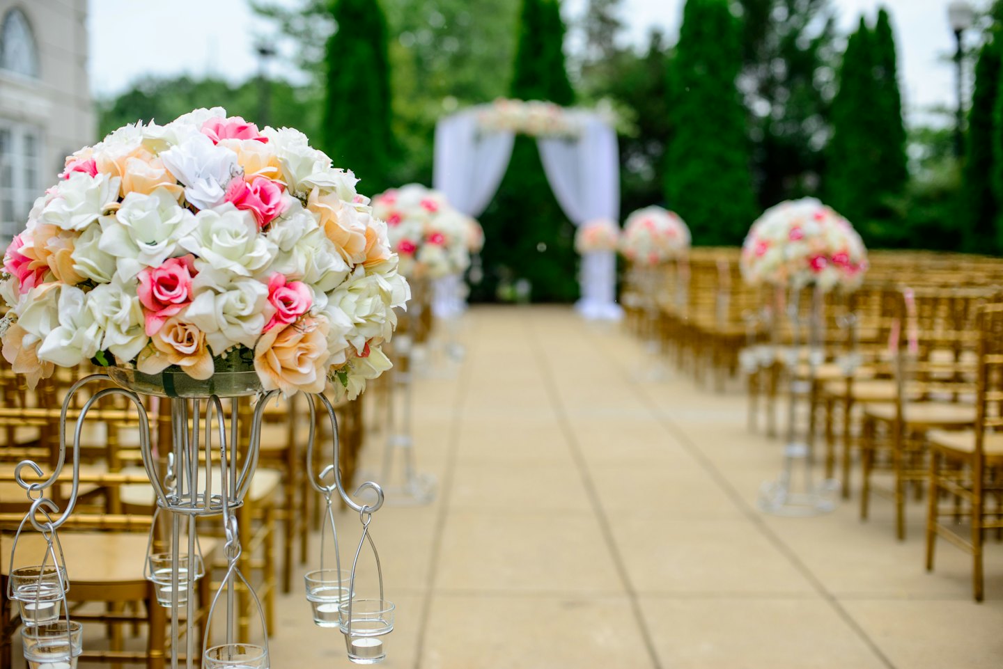 Golden chairs arranged for an outdoor wedding ceremony with floral arch.