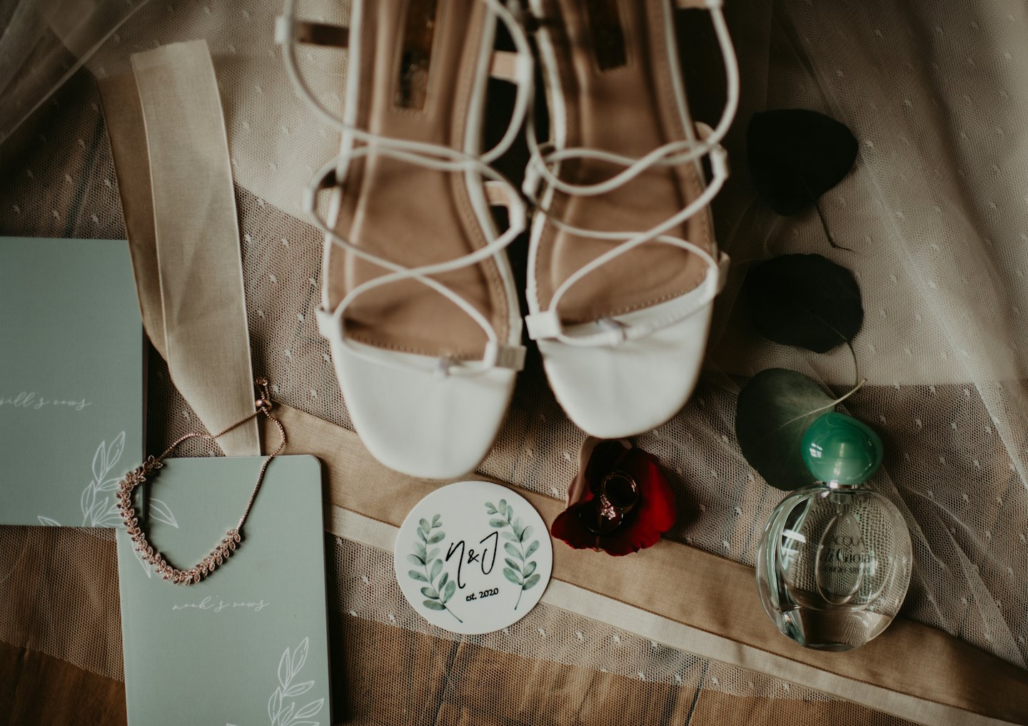 Bridal accessories arranged on lace fabric with shoes and vow booklets.