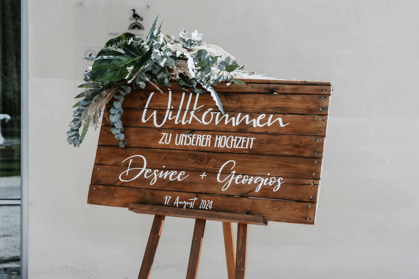 Wooden wedding welcome sign decorated with greenery on an easel.