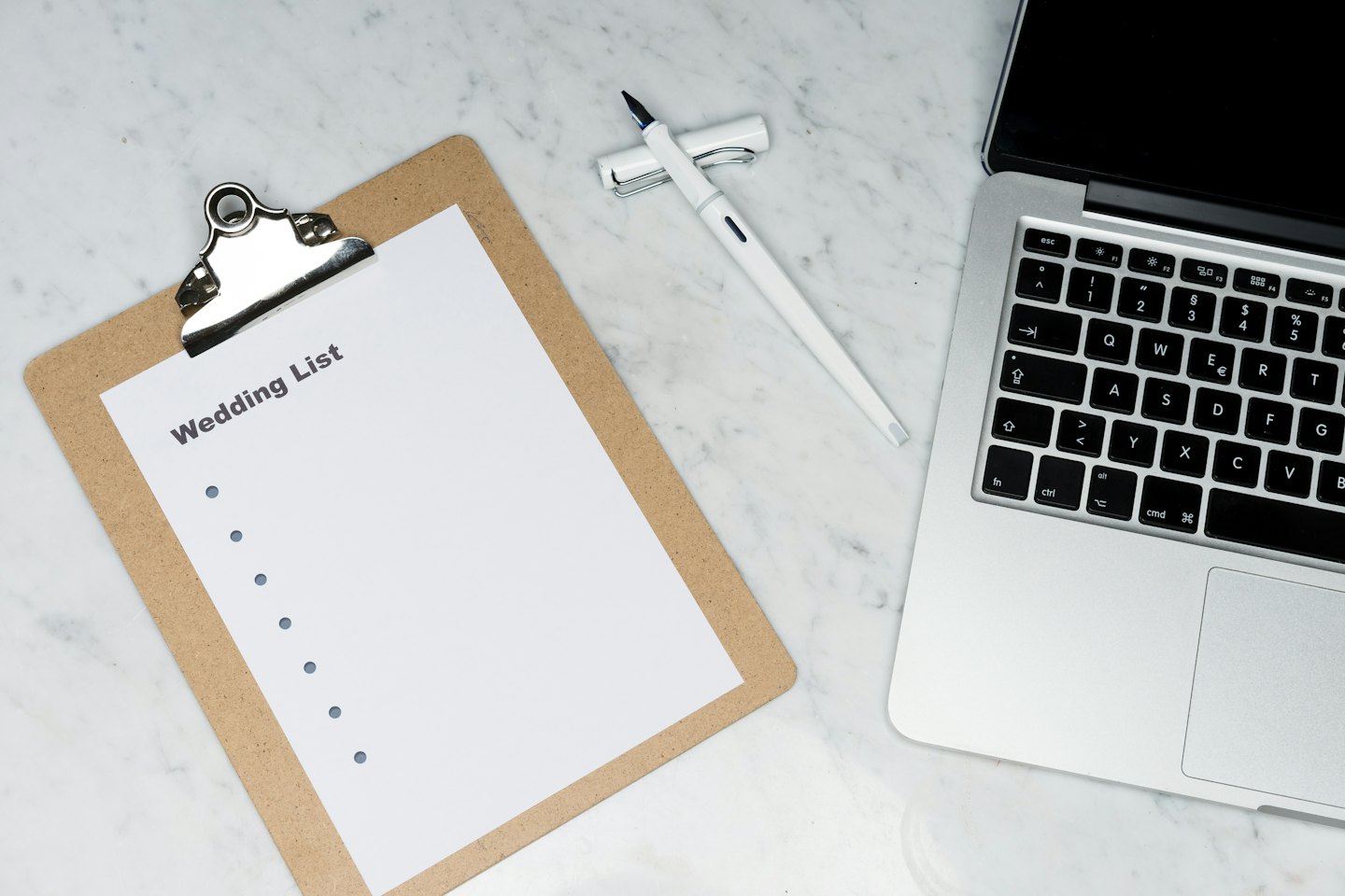 Wooden clipboard with wedding list, pen, and laptop.